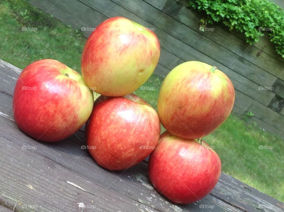 Apples stacked outdoors on wooden bench.