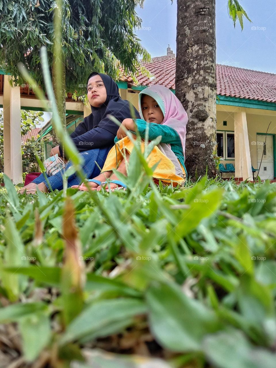 A teenager and a small child are relaxing under a tree.