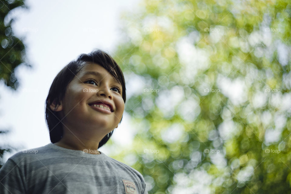 outdoor portrait of happy young eurasian boy on a blurry out of focus bokeh foliage background