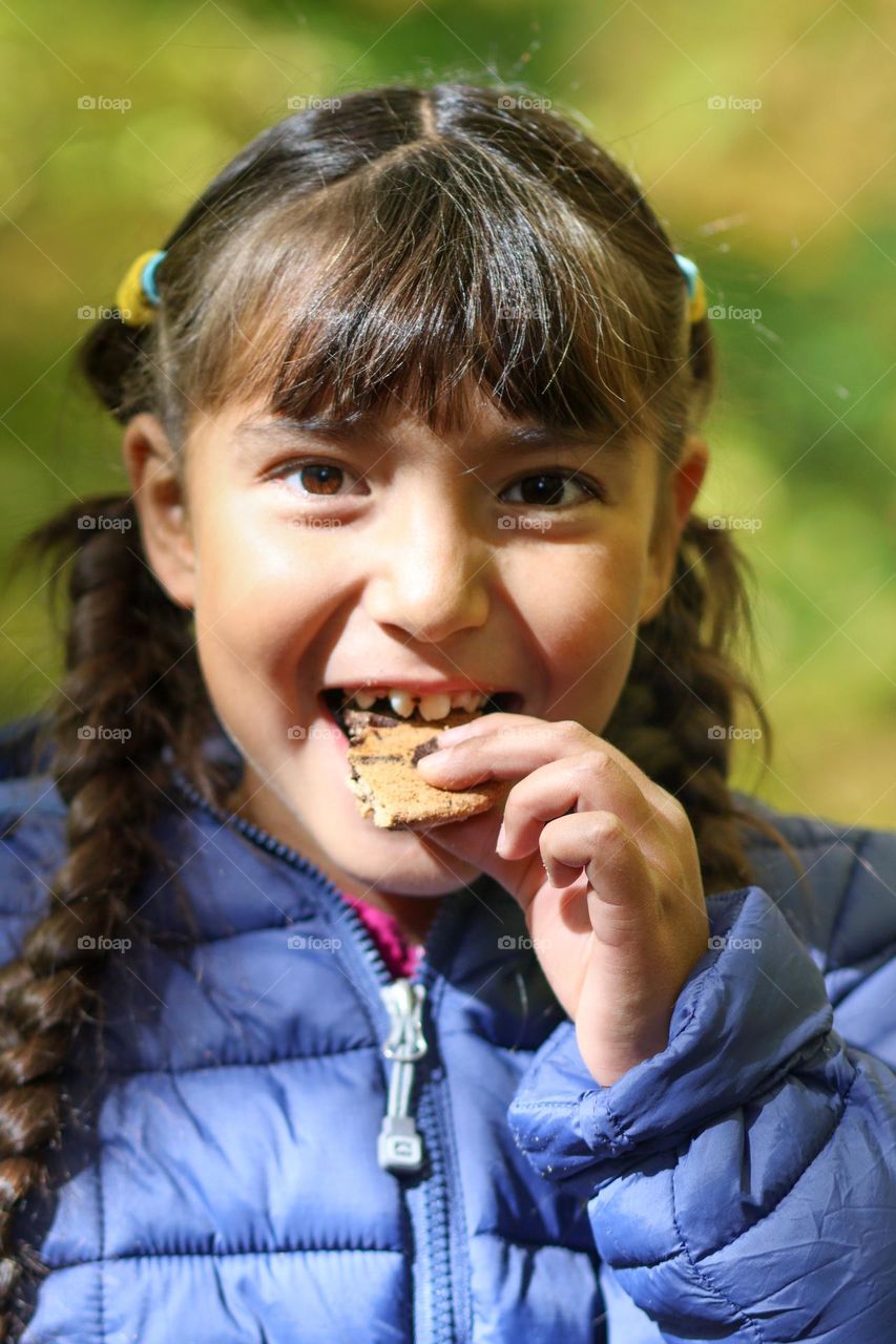 Cute girl is eating a cookie outdoors