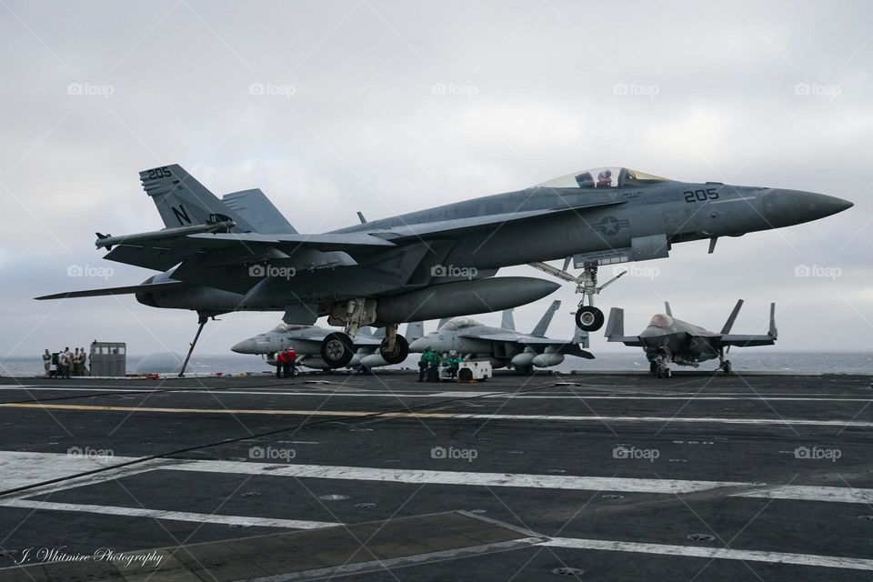 A F/A-18 Super Hornet prepares to land on a aircraft carrier deck
