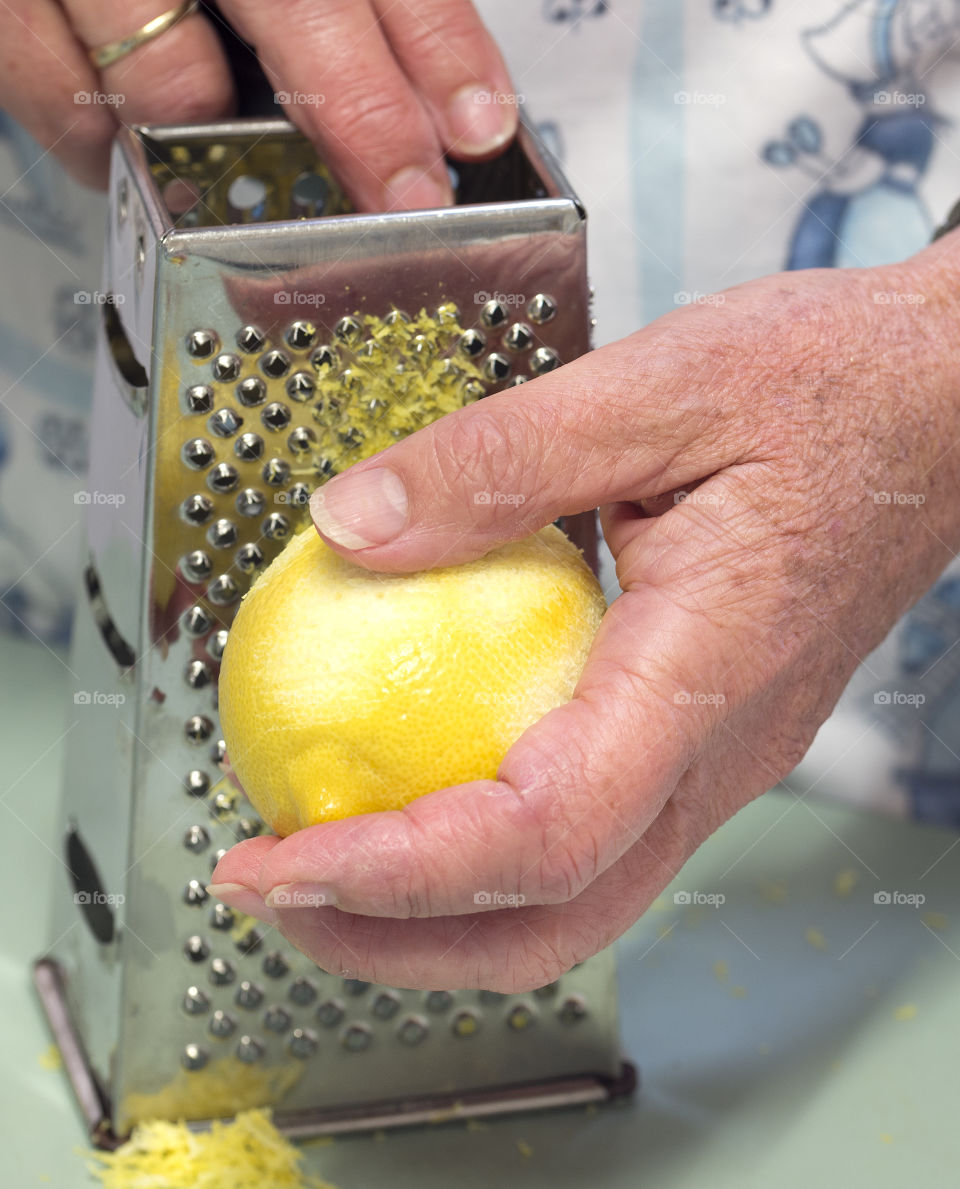 A woman's hand holds a lemon as it grated.