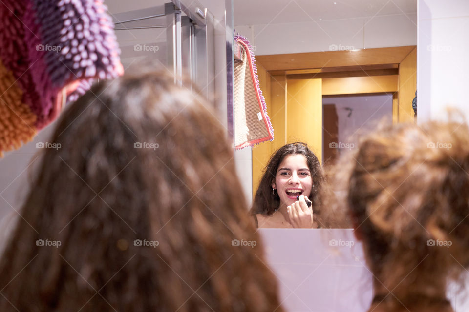 Rear view of woman looking at mirror and putting lipstick