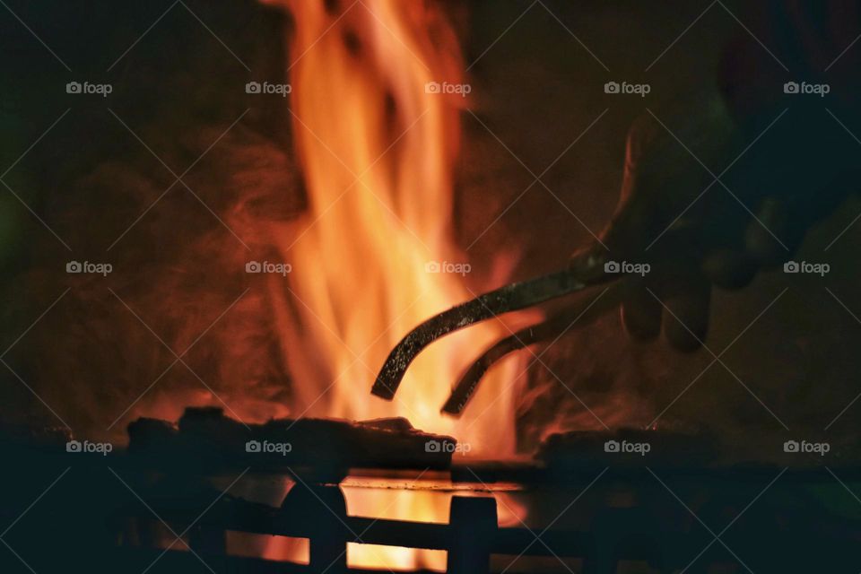 Close up of hand holding barbecue tongs over hot Fire