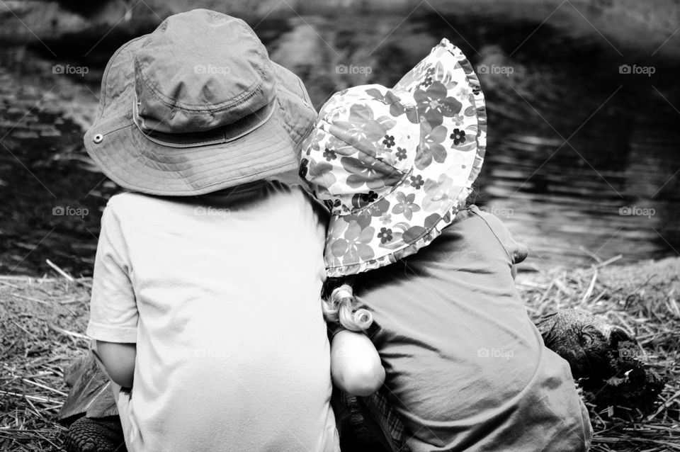 Black and White image of a young boy and girl sitting and cuddling together while overlooking a pond