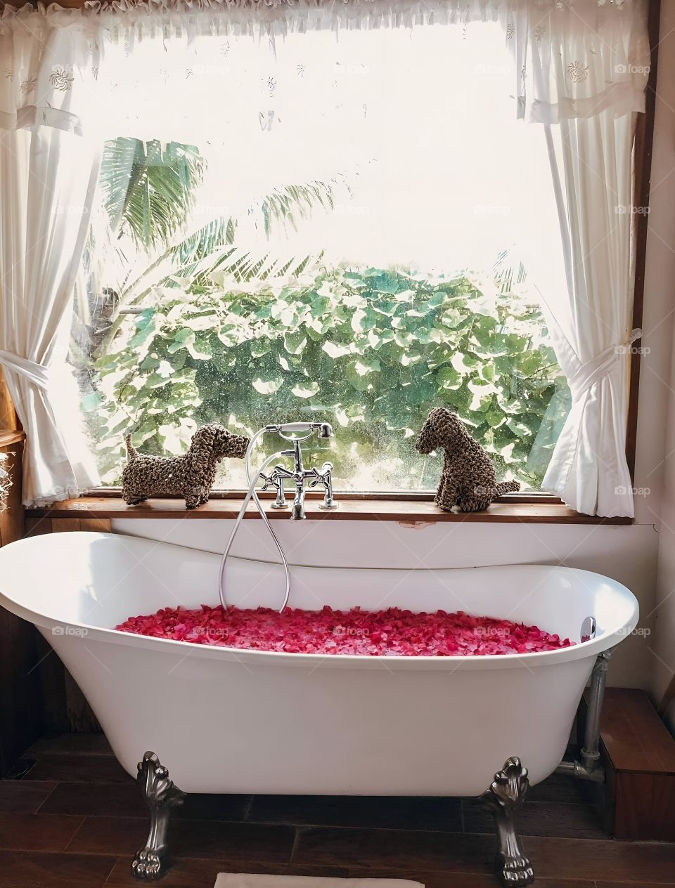 A bathtub strewn with rose petals by the window