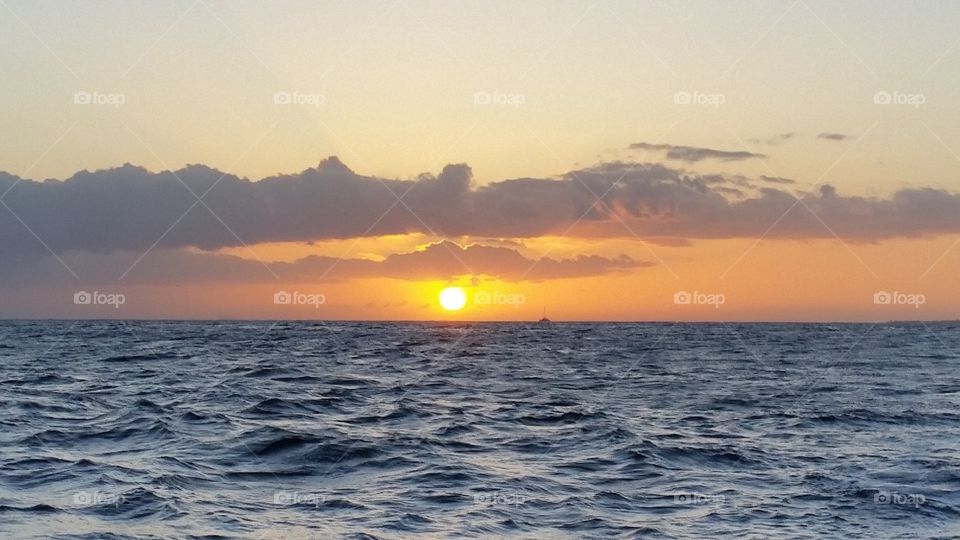 sunset in Hawaii, view from wavy ocean, sky and clouds with colors of yellow, orange, grey, and blue