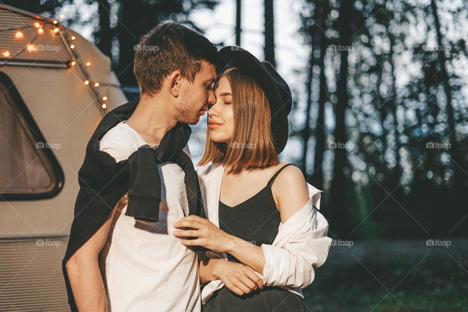 Young couple in love in stylish fashionable outfit romantic weekend wedding trip against background of camper in forest road trip