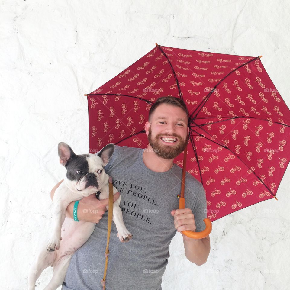 Love You Love People Umbrella Shot. Guy holding French bulldog with umbrella in front of white background