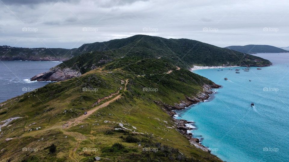 Cliff on the ocean in Arraial do Cabo, Brazil. Beautiful natural colors with blue ocean, waves that become foam, green hills.