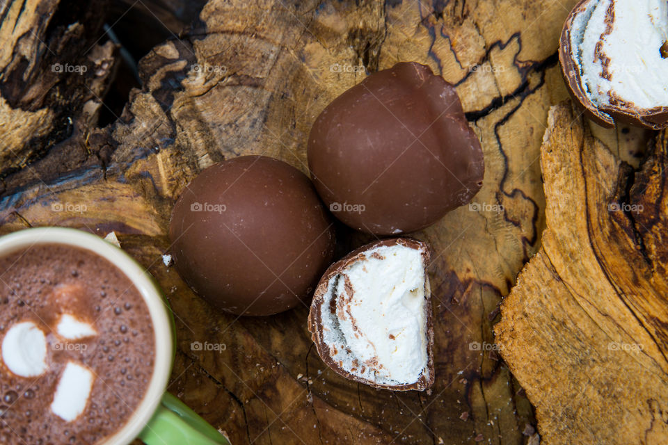 Delicious sweet hot chocolate with marshmallow and marshmallow filled chocolates on a wooden background. Flat lay close up of sweets chocolate and drink.