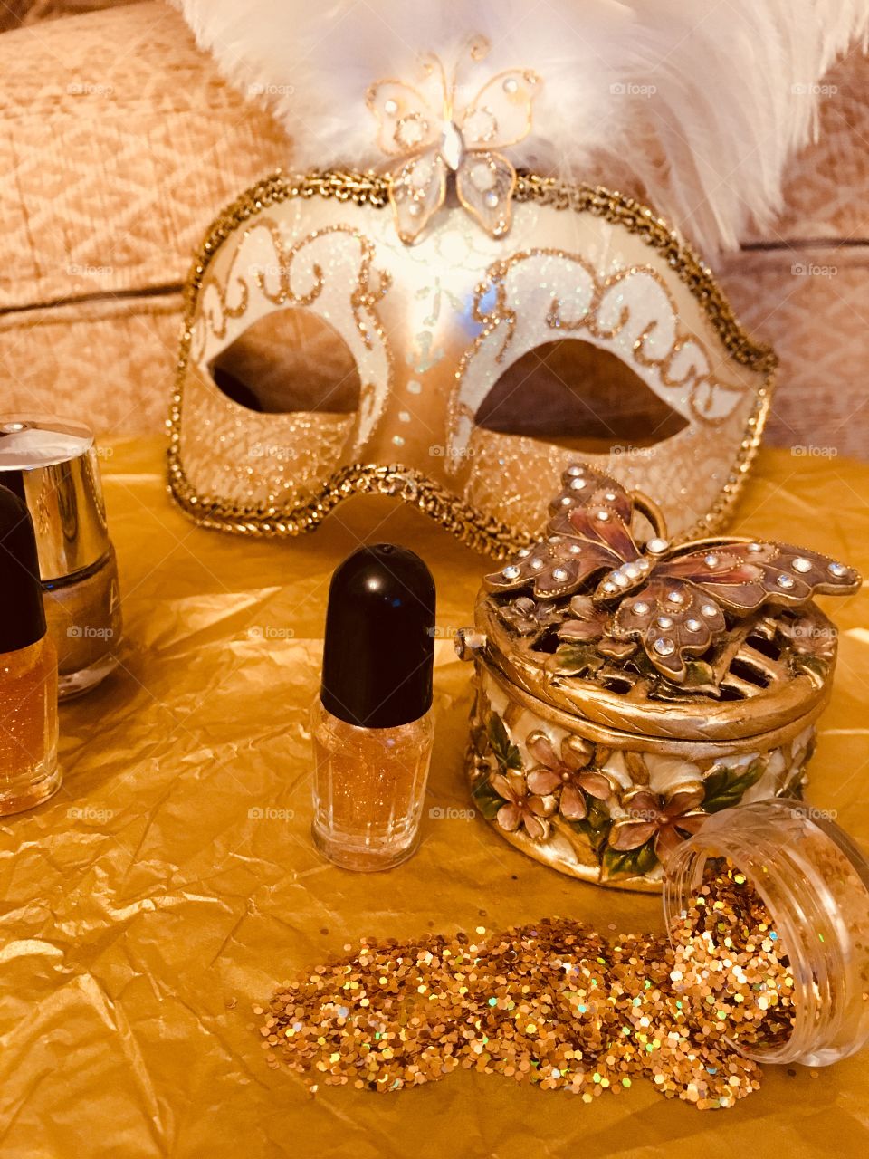 Gold nail glitter spilled with gold nail varnishes, butterfly trinket box and Venetian masquerade mask 