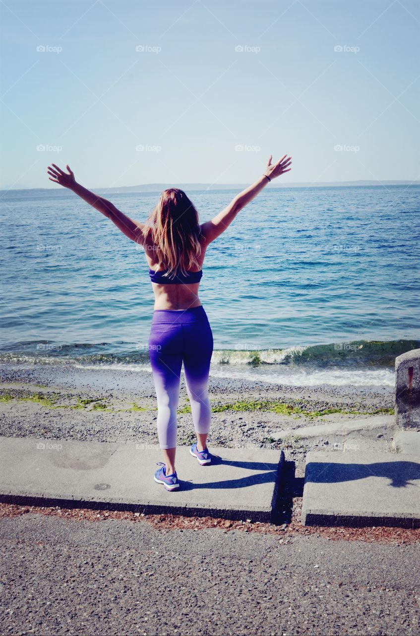 A woman celebrates fitness and health goals achieved on the puget sound of West Seattle.