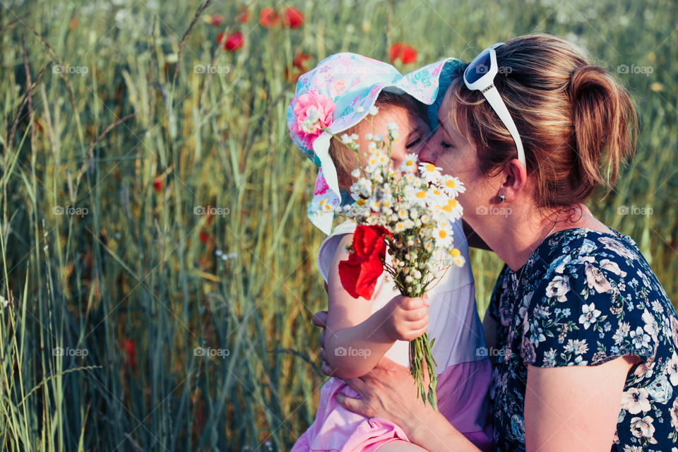Mother and her little daughter in the field of wild flowers. Little girl picking the spring flowers for her mom for Mother's Day in the meadow. Nature scene, family time