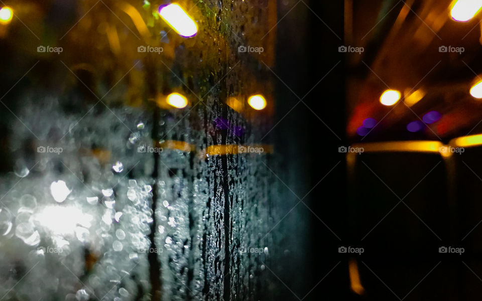 A wet glass window after hit by a rain at night, showing colorful light from outside