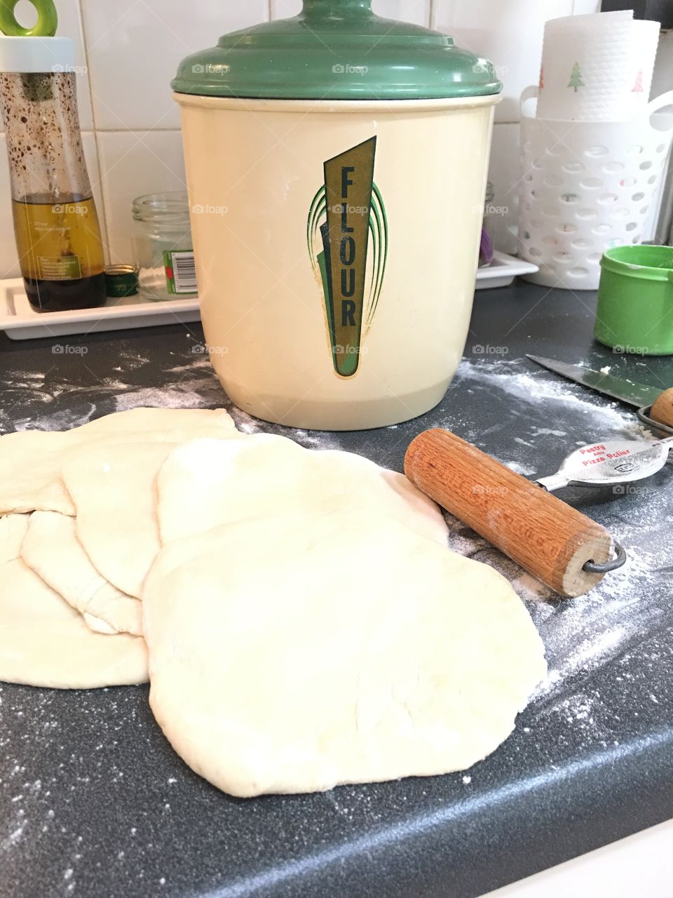 Rolling out the dough into circles for homemade pita bread, vintage 1940s flour canister bin in background 