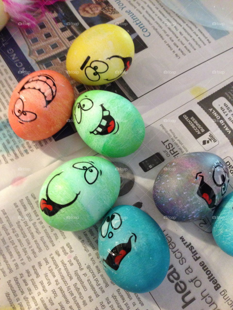 Homemade dyed Easter eggs with silly faces drying on a newspaper.  
