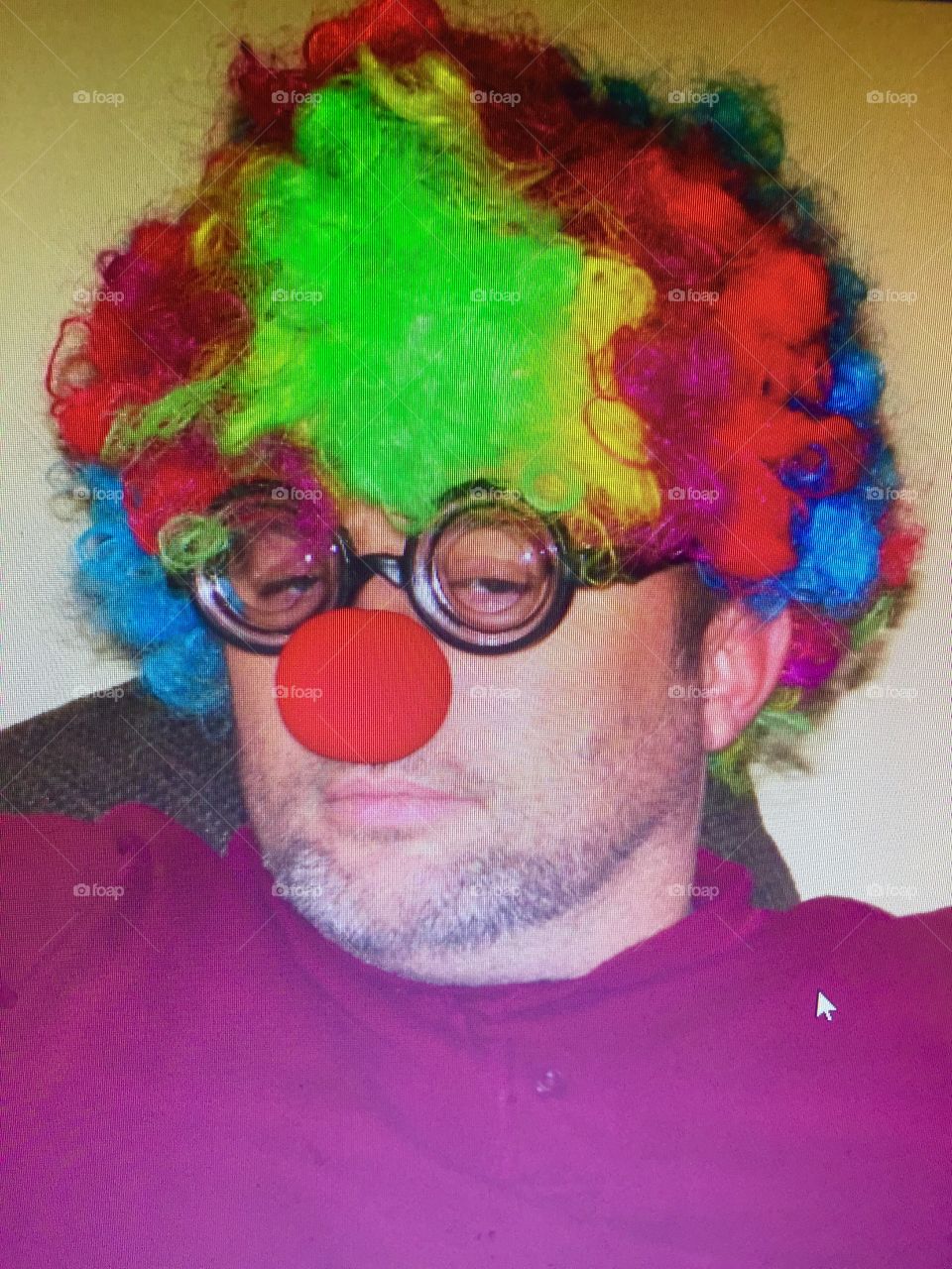Man dressed up in colored hair and red nose as a clown. Closeup of face.
