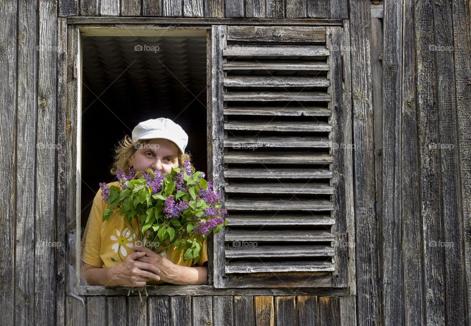 A woman on country house window, holding lilac flowers