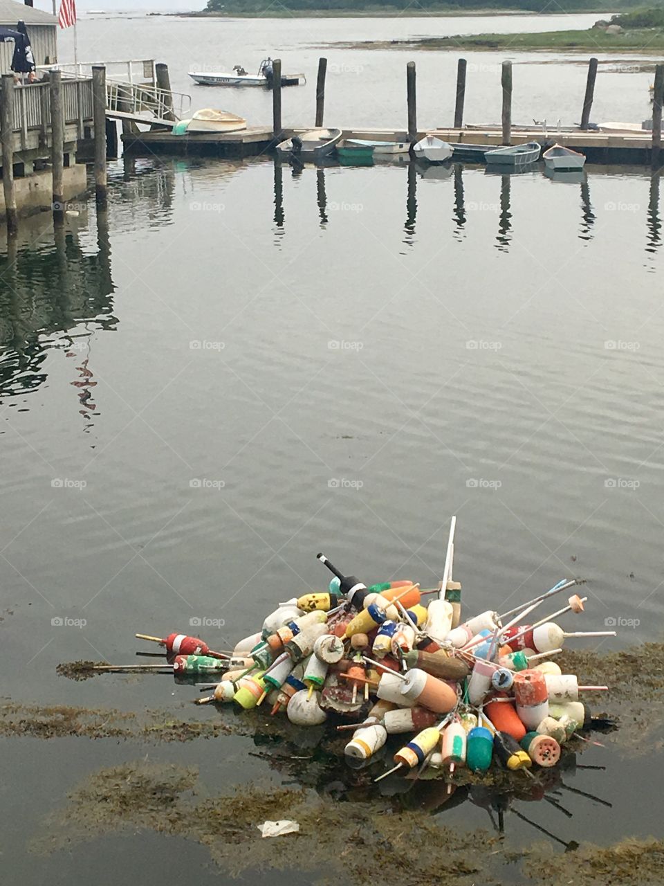 A cluster of lobster buoys sits in the shallow waters near a dock