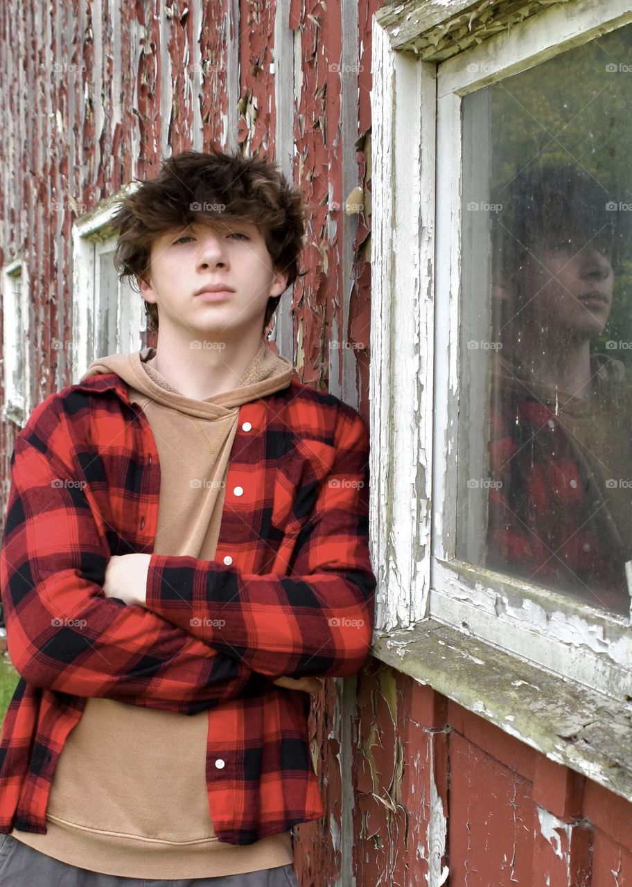 Young man leaning against an old building, his reflection in the window