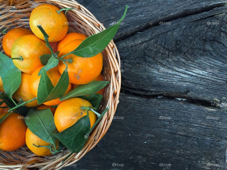 Wooden basket filled with mandarines and mandarine leaves on wooden table 