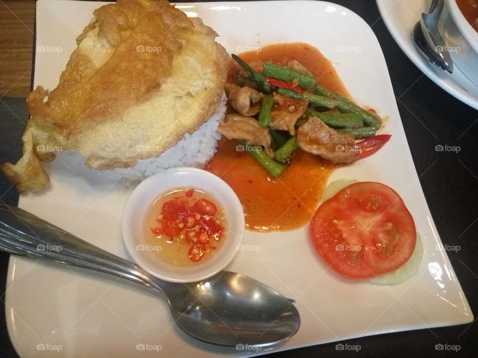 thai spicy pork, rice, omlete, a piece of tomato and salty sauce