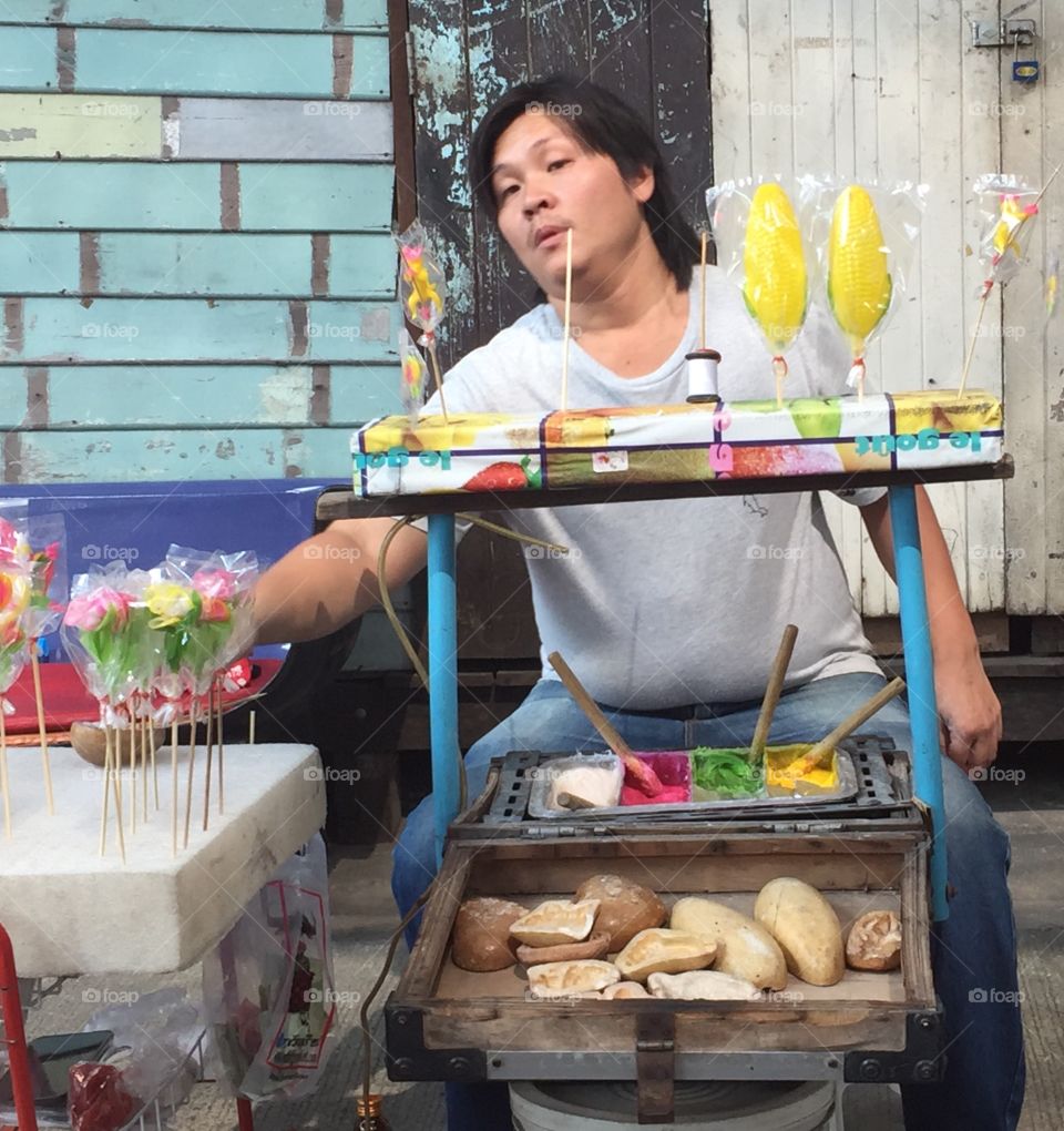 A street vendor outside one of the many temples we visited in Thailand, selling caramel confection with different colors and flavors. He used carved woods shown in front of his stall to give shape. He would also make sugar rose lollipops by hand.