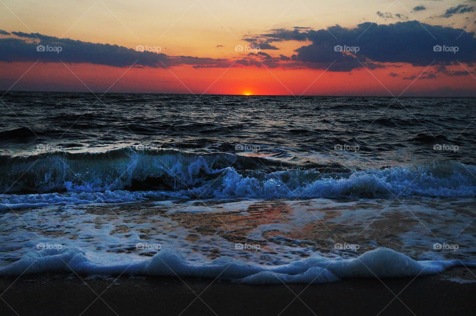 Waves crash on the shore of a beach during a vibrant sunset