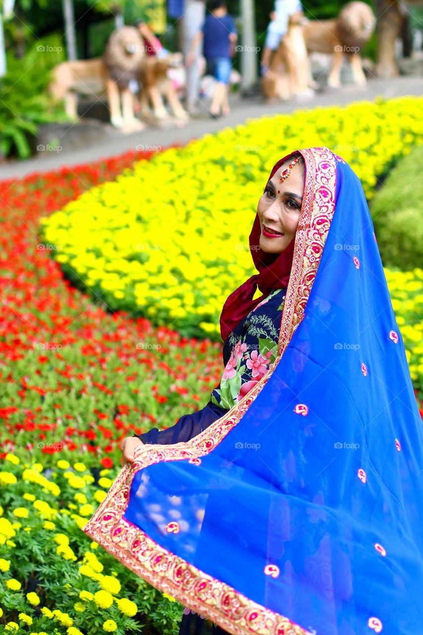 Portrait of a beautiful mother wearing a hijab, wearing a floral patterned robe and wearing black glasses, taking a photo with a happy expression.