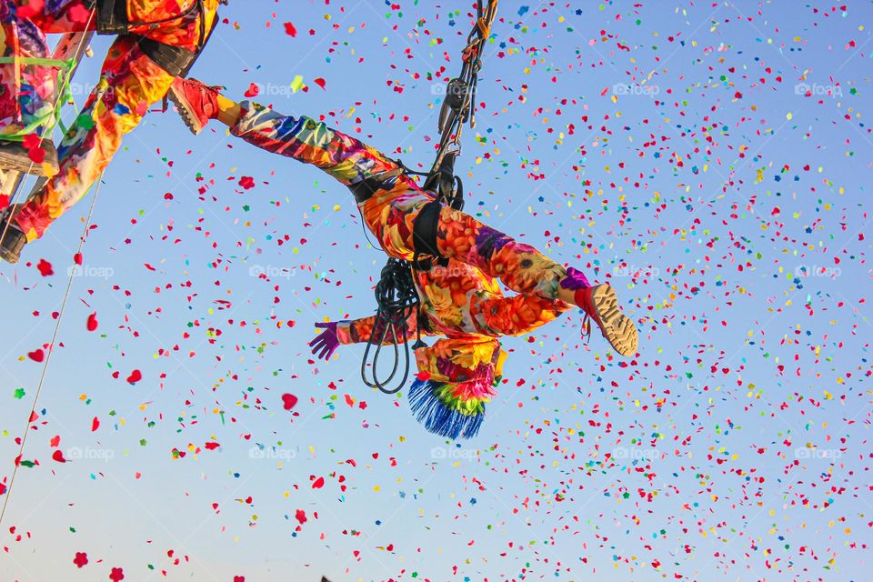 Acrobat girl in colored clothes performs a dance in the air against the backdrop of a blue sky and fireworks of sweets