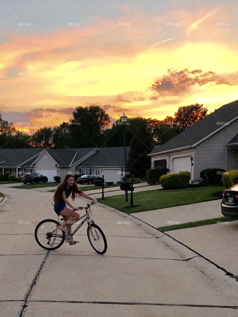 Girl riding bicycle on road during sunset in town