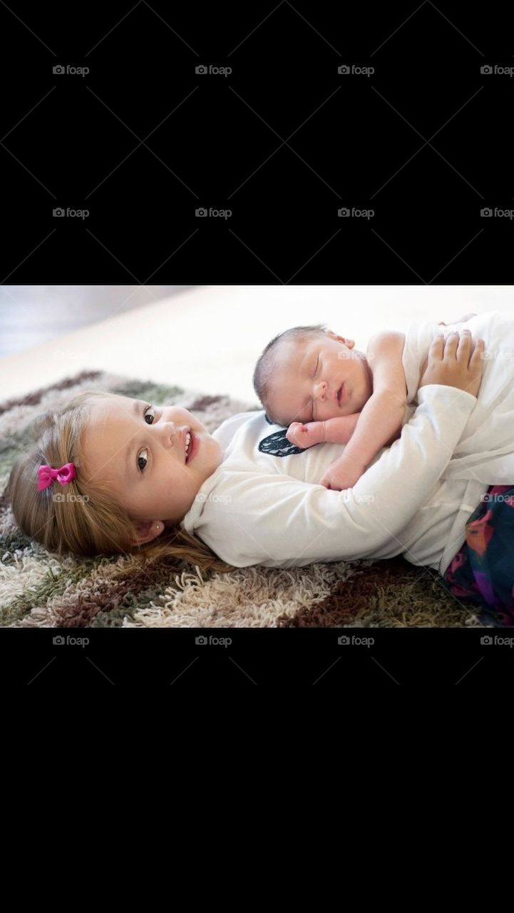 Sister holding her newborn brother on her stomach 