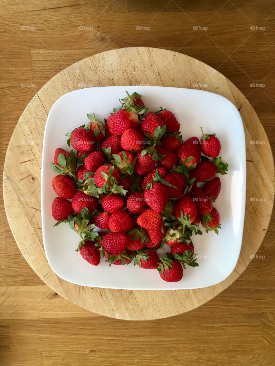 This is a photo of red strawberries on a white plate on a wooden table.