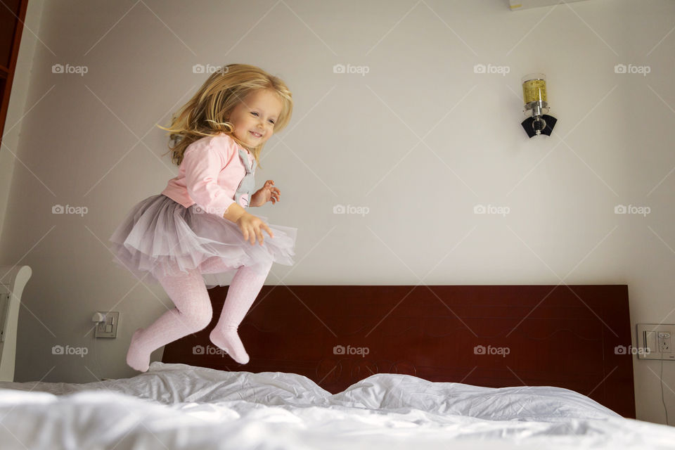 Happy little girl with blonde hair in tutu dress jumping on the bed 