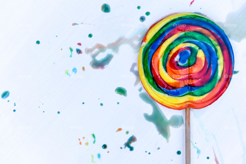 Flat lay of a rainbow swirl lollipop surrounded by colored sugar splatter