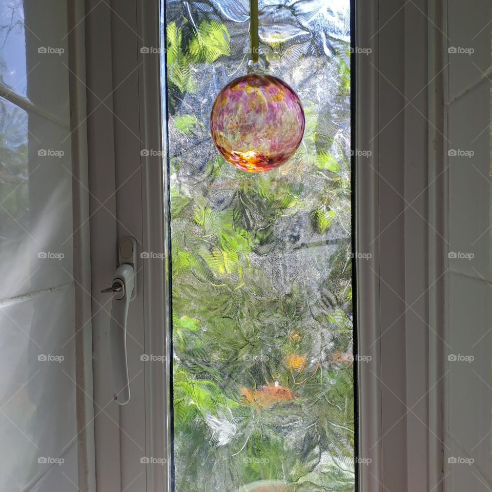 tiled wall with small window and natural daylight. glass ball hanging. daylight and green foliage outside