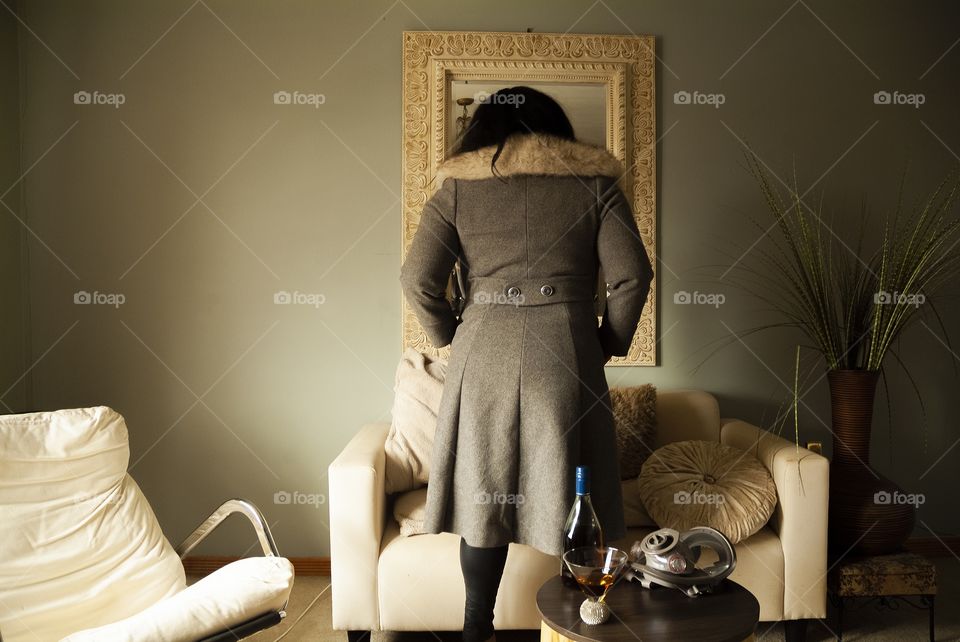 A woman tries on a coat in front of a mirror hanging on a bedroom wall.