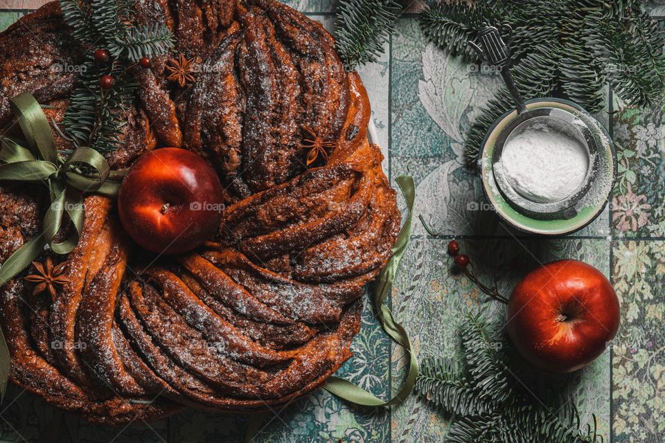 Chocolate cinnamon round wreath brioche with hole inside on the table decorated with apples