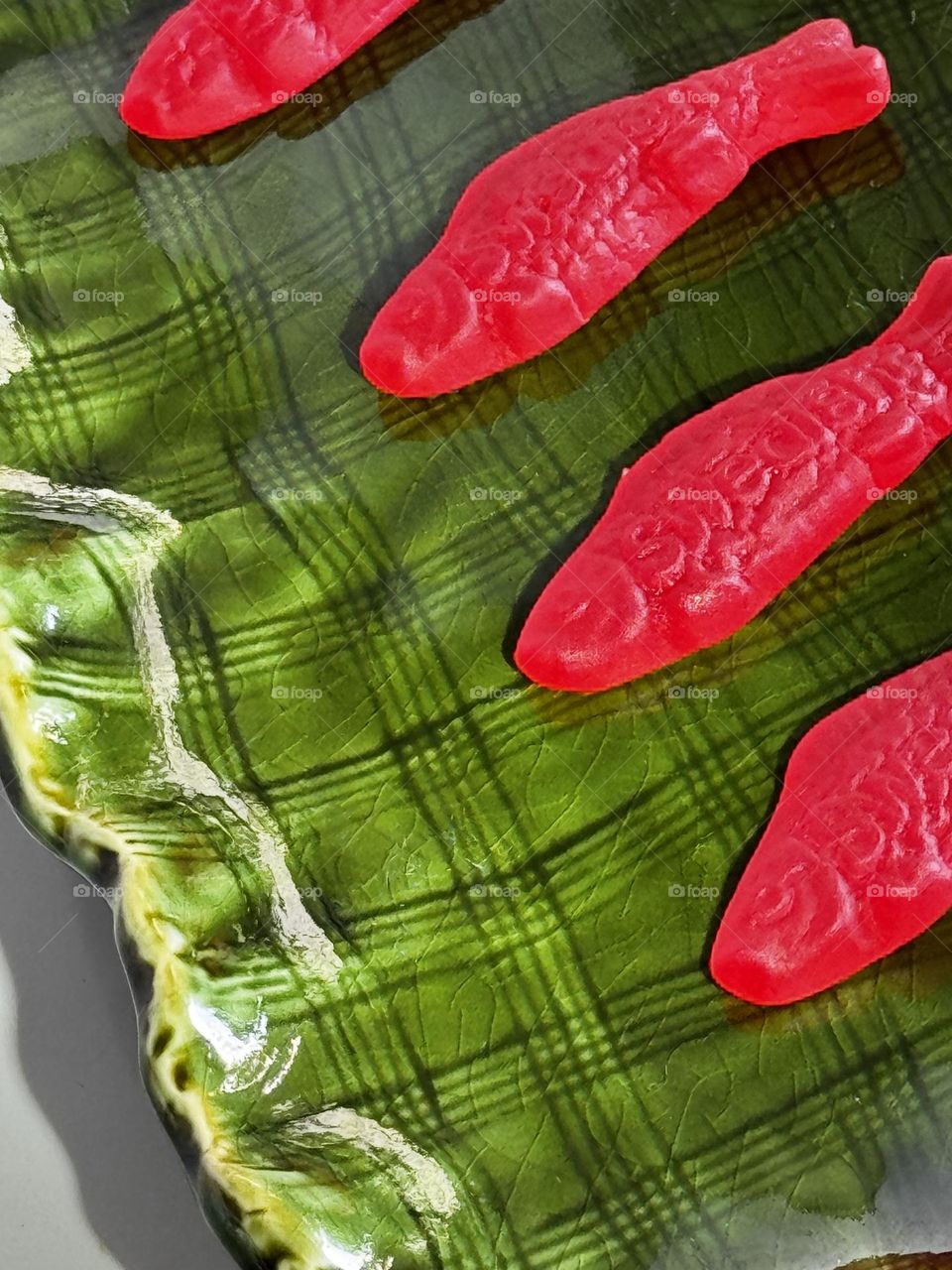 Four red Swedish fish candies on a handmade crackle-graze green plaid wavy edge ceramic dish 