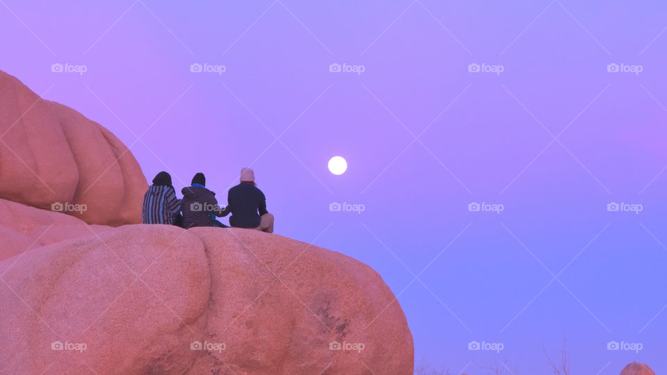 Full moon at sunset. Three girls watching the full moon at sunset in Joshua Tree Park, CA