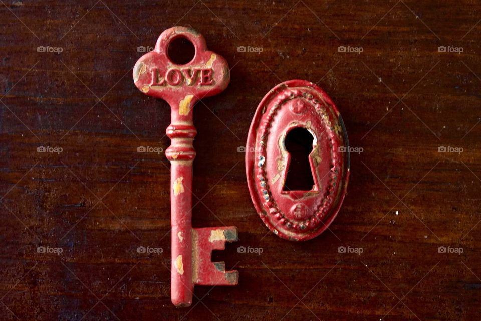 Red rustic vintage key with the word “LOVE” and keyhole on dark wooden surface