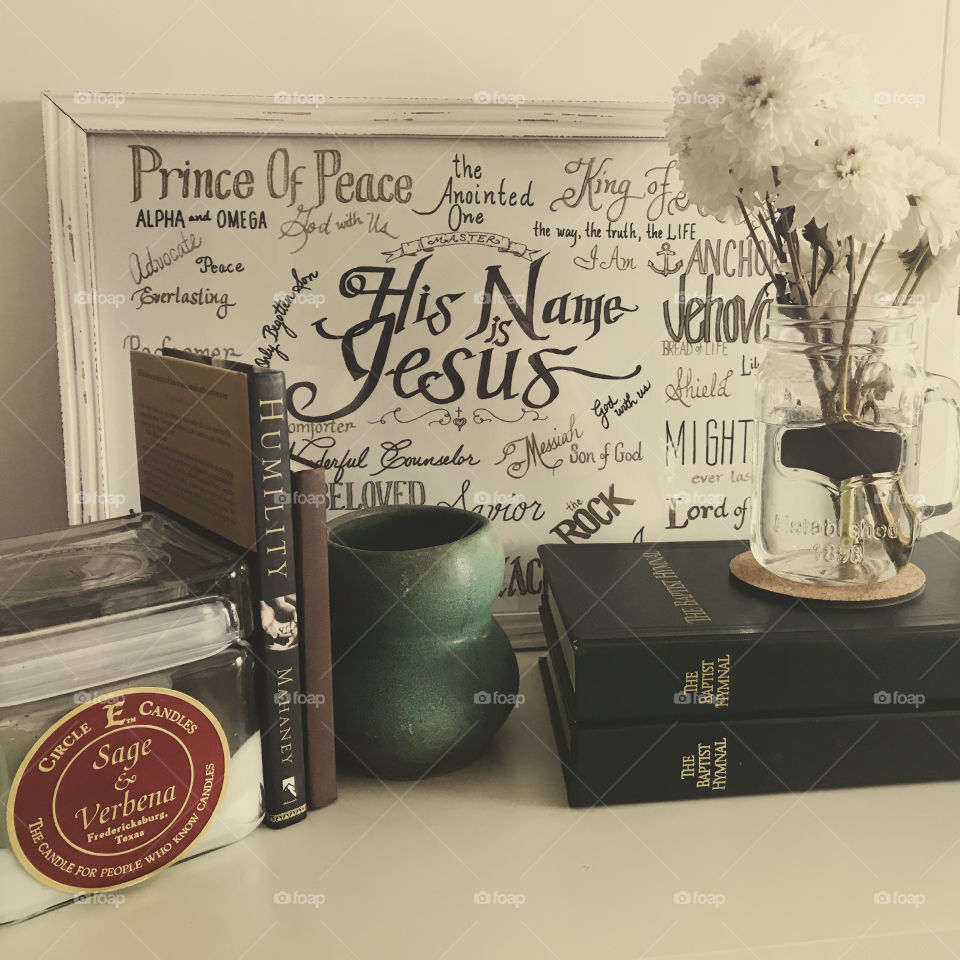 Christian word art, green Baptist hymnals, books, pottery, square Texas candle, jar of white flowers, displayed against white background