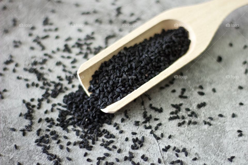 Overhead view of black seed spilling out of a wooden scoop on stone surface 