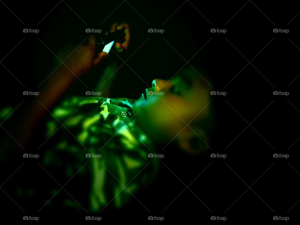 Littile child playing game on phone at night laying on bed.