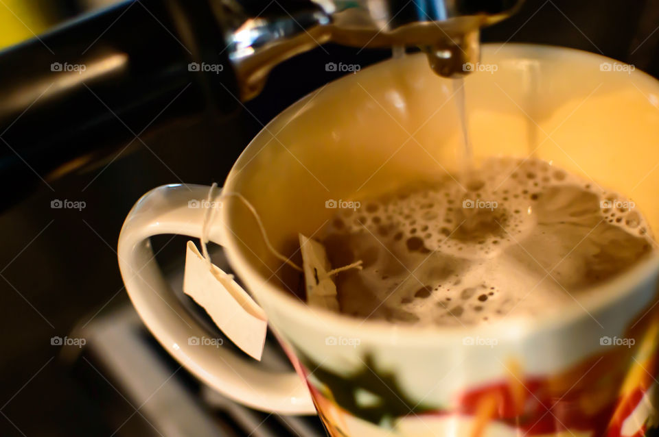 Making cup of tea closeup shot of water pouring into mug with tea bag from espresso machine background 