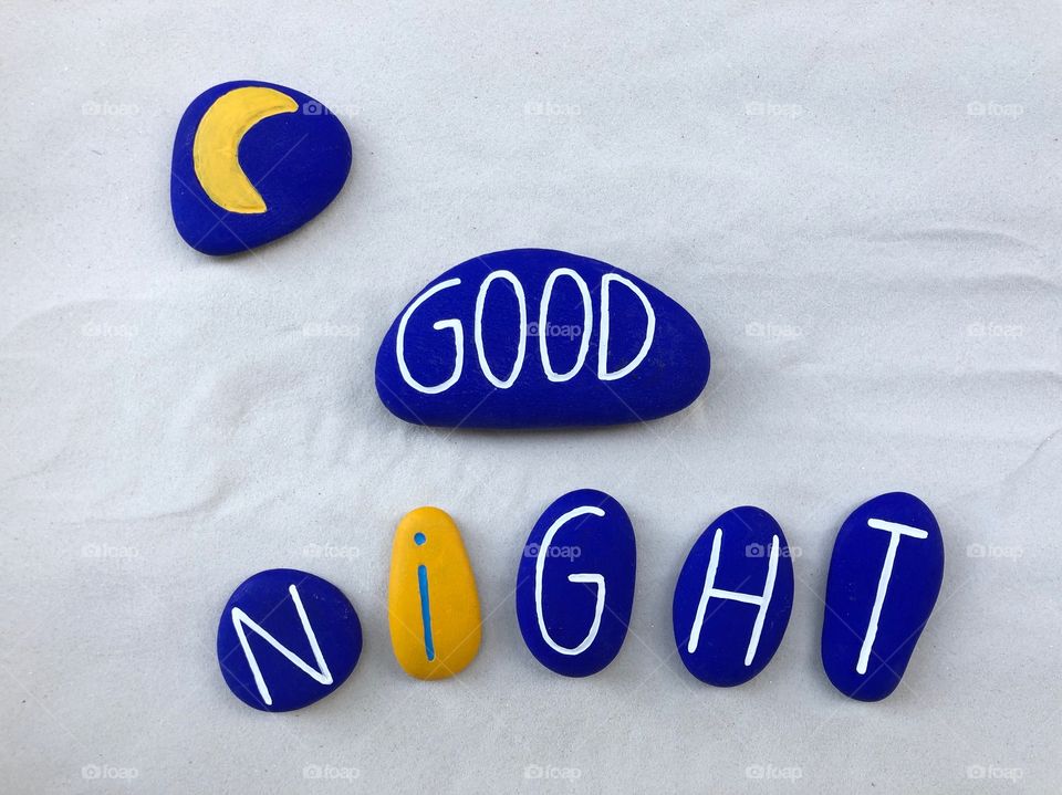 Good night text with blue and yellow painted stones over white sand