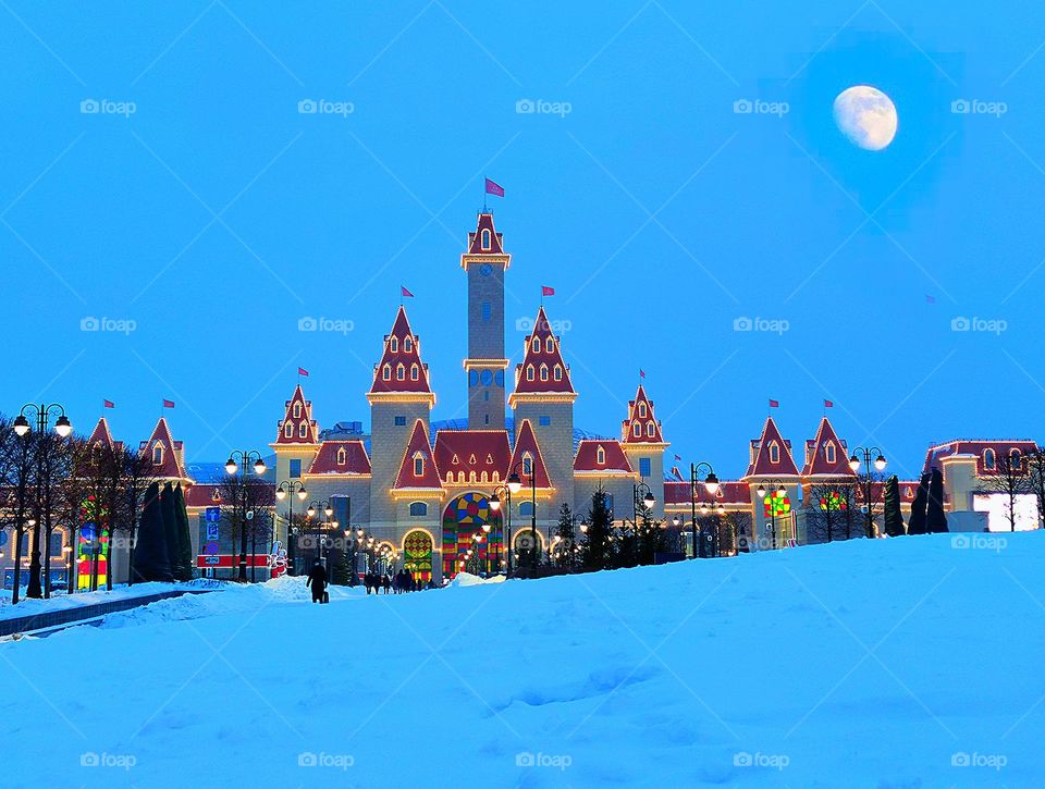 A glowing castle in the snow, with the moon shining above it.Winter evening