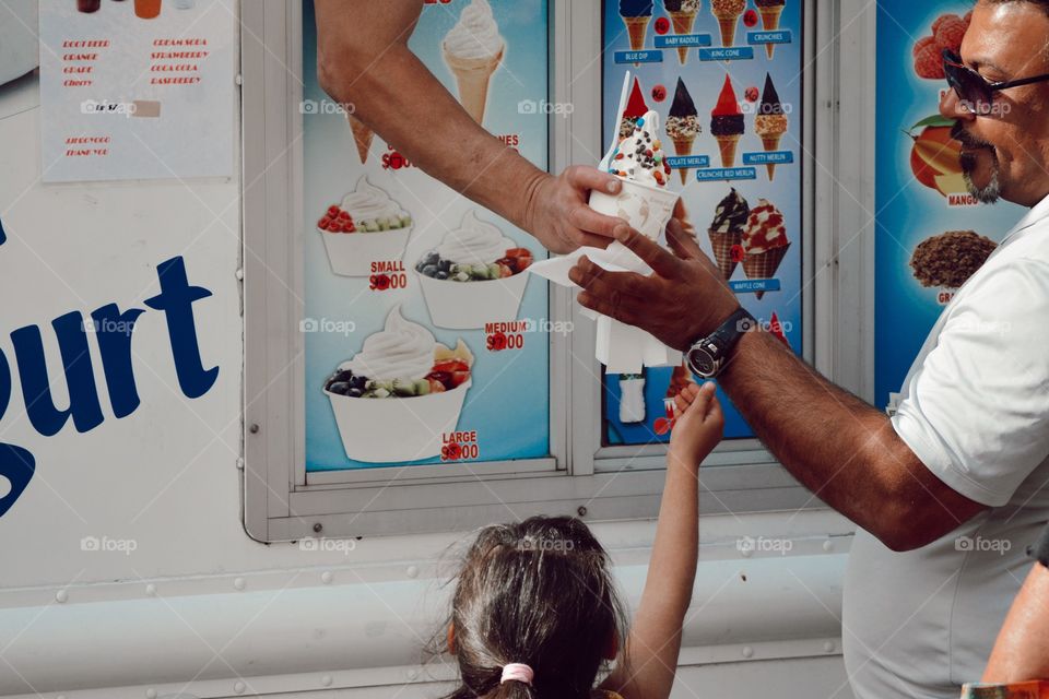 ice cream truck man hanging vanilla ice cream with chocolate and sprinkles to a little girl, who reaches her arm up 