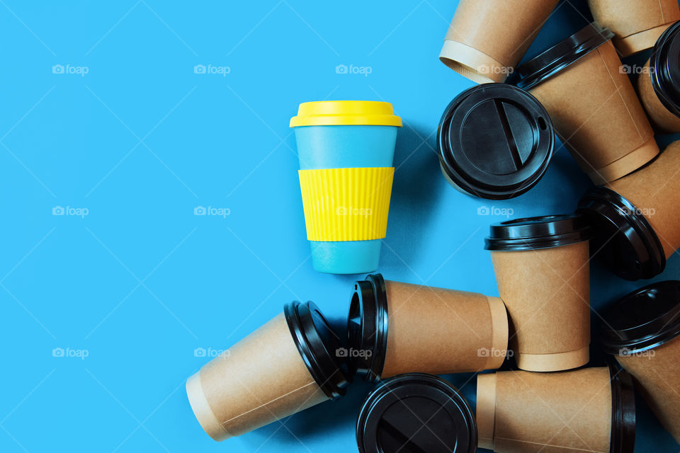 Zero waste concept. Stylish reusable eco coffe cup and multiple single use cardboard cups.Ban single plastic. Sustainable lifestyle,flat layout on blue background. 